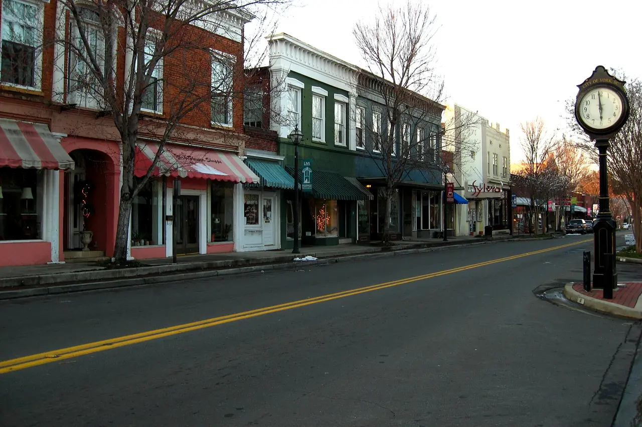 Brick storefronts with striped awnings along a street in downtown York, SC, beside a City of York street clock